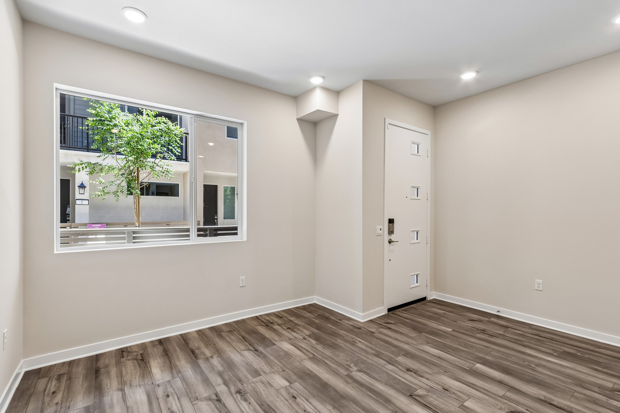 A room with a wood floor and a window with a plant in it.