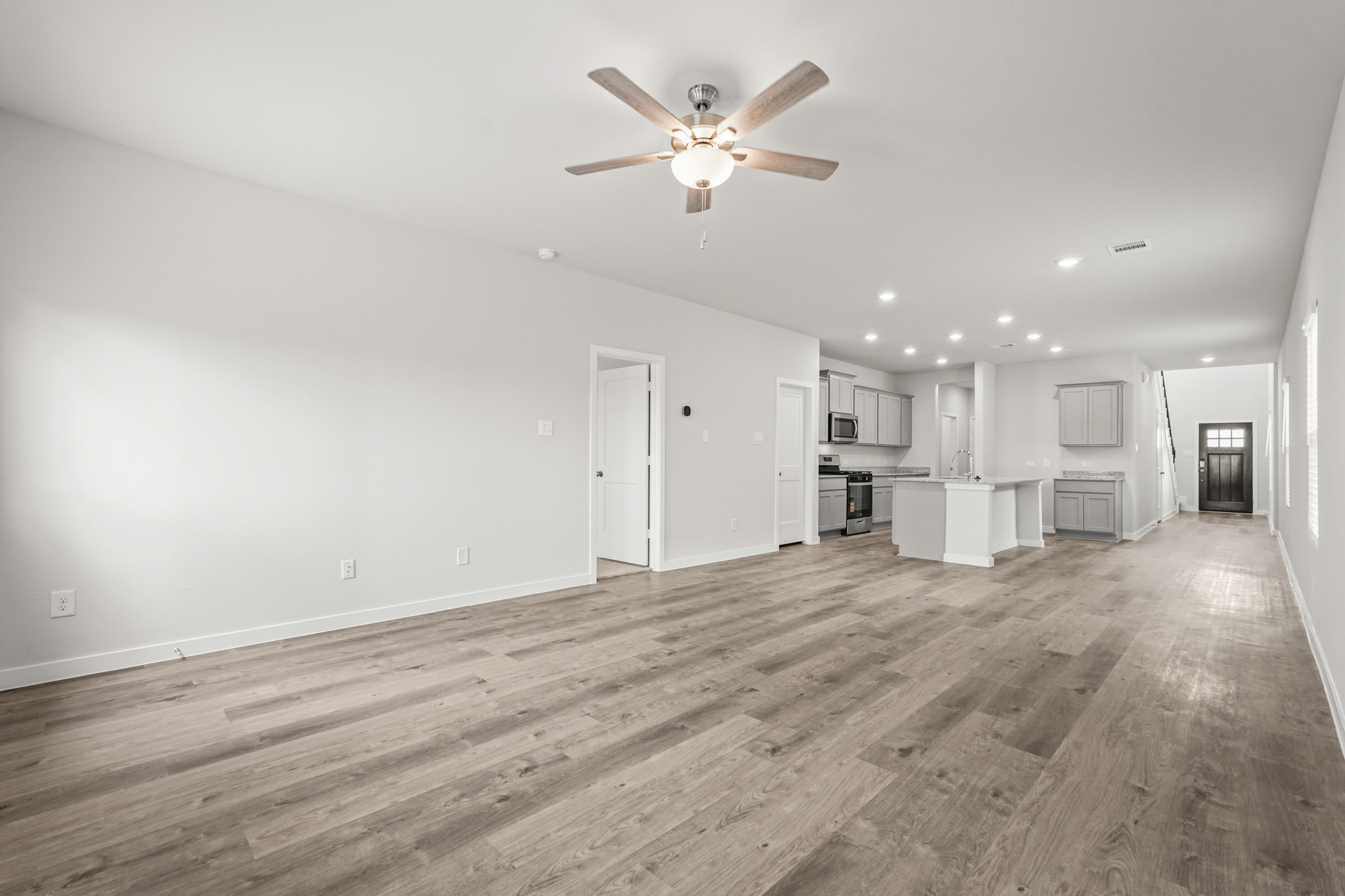 A large empty room with a ceiling fan and wood floors.